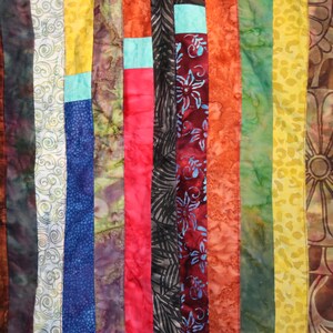 K&ouml;nnte beinhalten: Eine bunte Stoffdecke mit vertikalen Streifen in verschiedenen Rot-, Orange-, Gelb-, Gr&uuml;n-, Blau- und Lilat&ouml;nen. Der Stoff ist mit Spiralen, Blumen und geometrischen Mustern gemustert.