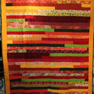 Könnte beinhalten: Ein farbenfroher Quilt mit einem horizontalen Streifenmuster. Der Quilt besteht aus verschiedenen Stoffen in Rot-, Orange-, Gelb-, Grün- und Brauntönen. Der Quilt ist mit einem einfachen Steppmuster gesteppt.