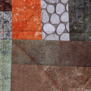 Puede incluir: Primer plano de una colcha de retazos marr&oacute;n, verde y naranja con un patr&oacute;n geom&eacute;trico. La colcha est&aacute; hecha de diferentes telas con diversas texturas y dise&ntilde;os.