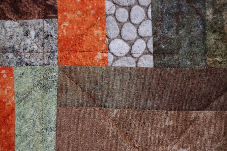 Puede incluir: Primer plano de una colcha de retazos marr&oacute;n, verde y naranja con un patr&oacute;n geom&eacute;trico. La colcha est&aacute; hecha de diferentes telas con diversas texturas y dise&ntilde;os.