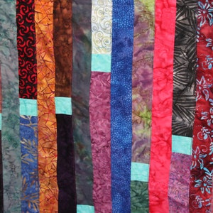 K&ouml;nnte beinhalten: Ein farbenfroher Quilt aus Stoffstreifen in verschiedenen Mustern und Farben, darunter Rot, Orange, Gelb, Gr&uuml;n, Blau, Lila und Braun. Der Quilt besteht aus vertikalen Stoffstreifen, wobei einige horizontale Stoffstreifen dazwischen eingen&auml;ht sind.