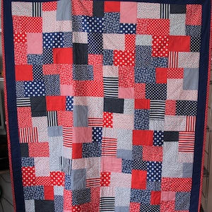 Könnte beinhalten: Eine rot-weiß-blaue Patchwork-Decke mit verschiedenen Mustern, darunter Punkte, Gingham und Paisley.