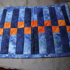 Könnte beinhalten: Ein blauer und orangefarbener gesteppter Tischläufer mit geometrischem Muster. Der Läufer ist aus Stoff mit Marmormuster.