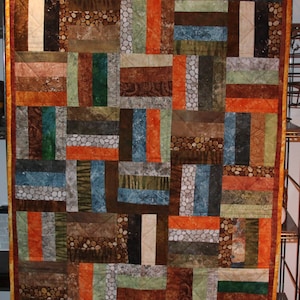 Könnte beinhalten: Ein Quilt aus verschiedenen Stoffresten in Braun-, Orange-, Grün- und Blautönen. Der Quilt besteht aus horizontalen und vertikalen Stoffstreifen, die ein Patchwork-Muster bilden.