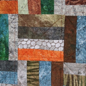 Puede incluir: Una colcha de retazos con una variedad de telas marrones, naranjas, verdes y azules. Las telas tienen diferentes patrones, incluyendo piedras, rayas y veta de madera.
