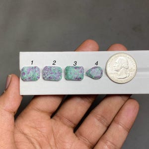 May include: Four loose gemstones with a mottled green and magenta pattern, labelled 1 through 4, displayed on a white card next to a United States quarter coin for scale. Three stones are rectangular, and one stone is pear-shaped.