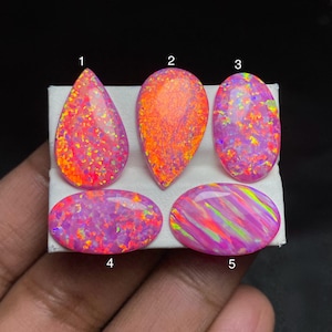 May include: Five opals in different shapes: teardrop, oval, and pear. The opals display a mix of colours, including pink, orange, and green, with a shimmering, iridescent effect. The gemstones are set against a white background.