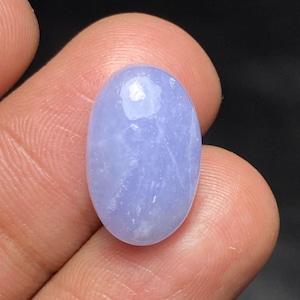 Könnte beinhalten: Ein ovaler, polierter blauer Chalcedon-Edelstein mit einer glatten Cabochon-Oberfläche. Der Stein zeigt eine durchscheinende, hell-periwinkle-blaue Farbe mit feiner weißer Maserung im Inneren und einer glänzenden, reflektierenden Oberfläche.