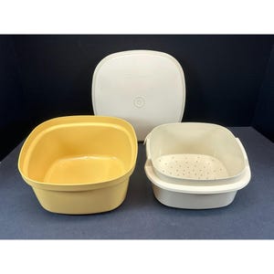 May include: A set of vintage Tupperware containers in cream and yellow. The set includes a square-shaped container, a perforated insert, and a lid. The containers are made of durable plastic and are designed for food storage.