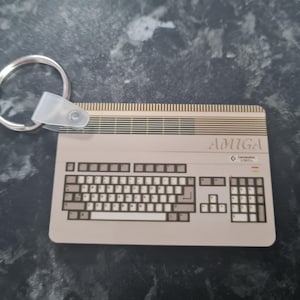 May include: A white and grey keychain shaped like an Amiga computer with a keyboard and the word "AMIGA" printed on the top.