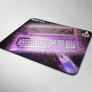 Puede incluir: Un ordenador Atari ST morado con un teclado blanco y un fondo de cuadros blancos y negros. El logotipo de Atari está en la esquina superior derecha de la imagen.