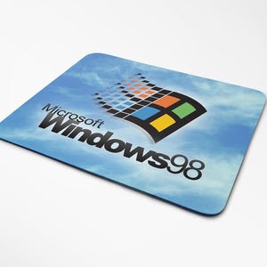 Peut inclure: Tapis de souris rectangulaire avec le logo Microsoft Windows 98 sur fond de ciel bleu. Le logo comprend le symbole Windows avec des carrés orange, jaune, vert et bleu. Le texte "Microsoft Windows98" est imprimé en noir.