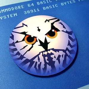 Pode incluir: Gráfico circular branco e azul com o rosto de uma coruja e olhos laranja. A imagem está sobre um fundo azul com texto de um computador Commodore 64.