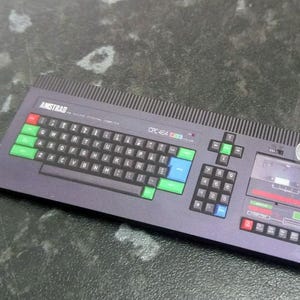 May include: A black and gray vintage computer keyboard with a cassette tape drive. The keyboard has green and blue keys and the text "ASTRAD CPC 464" is printed on the top.