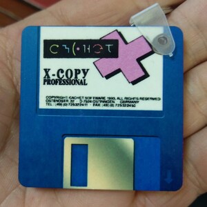 May include: Blue floppy disk with a pink plus sign and the text "C( )HET X-COPY PROFESSIONAL COPYRIGHT: CACHET SOFTWARE 1990, ALL RIGHTS RESERVED OSTENDSTR 32 D-7524 OSTIRINGEN GERMANY TEL: (49) (0) 725322411 FAX (49) (0) 725322450".