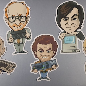 May include: Set of seven colourful cartoon character magnets featuring men with different hairstyles and facial expressions. Each magnet has a retro computer or keyboard in their hands. The magnets are on a silver surface.