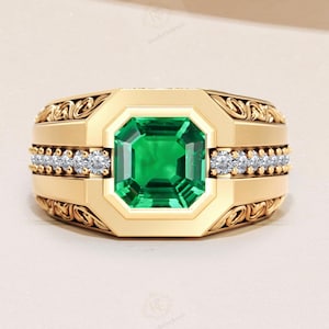May include: A gold ring with a large, square-cut emerald center stone. The ring has a decorative design on the sides and a row of small diamonds on each side of the emerald. The ring is a classic, elegant design.
