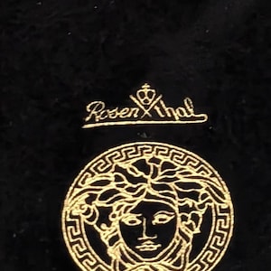 May include: Black velvet bag with gold embroidery. The bag features the Versace logo, a gold circle with a Medusa head and the word "VERSACE" written below.