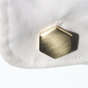 Puede incluir: Un botón de camisa hexagonal de oro con acabado cepillado.