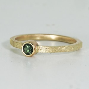 Könnte beinhalten: Ein goldener Ring mit einer strukturierten Band und einem kleinen grünen Edelstein.