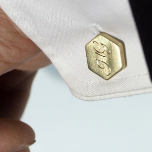 Puede incluir: Gemelos de oro con forma hexagonal y la palabra "Big" grabada en la parte delantera.