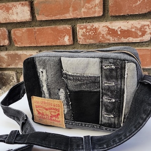 Puede incluir: Bolso bandolera de mezclilla negra y gris con cierre de cremallera y correa ajustable. El bolso está hecho de mezclilla patchwork y presenta una etiqueta Levi Strauss & Co.