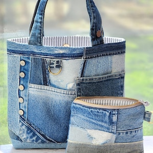 May include: A denim tote bag and a matching zippered pouch. The bag features a patchwork design, button details, and a gold-tone ring. The pouch has a zip closure and a striped lining. Both items are crafted from recycled denim.