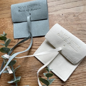 May include: Two small, fabric gift bags with a drawstring closure. The bags are made of a soft, suede-like material. The blue bag has the text "To my beautiful Maid of Honor" printed on the front. The white bag has the text "To my beautiful Maid of Honor" printed on the front.