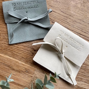 May include: Two small, fabric gift bags with a satin ribbon tie. The bags are light gray and white and have the text "To my beautiful bridesmaid" embossed on the front.