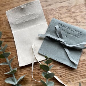 May include: Two small, fabric gift bags. One is white with a subtle embossed design and the other is light blue with the text "To my beautiful bridesmaid" in black.