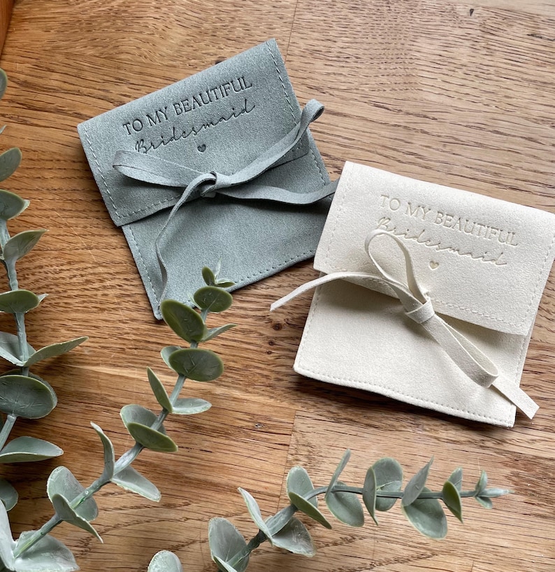 Fabric gift bags with a drawstring closure. The bags are made of a soft, suede-like material. The bags are available in sage green, blush pink and off-white. The bags are decorated with the text "To my beautiful bridesmaid" in a cursive font.