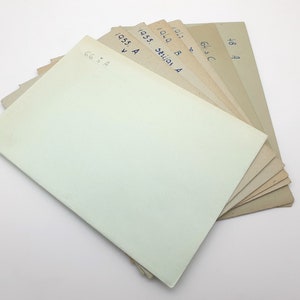 Pode incluir: Uma pilha de oito folhas de papel de cores diferentes com números e letras escritas à mão em cada folha. A folha superior é de cor verde claro.