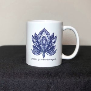 Peut inclure: Une tasse en c&eacute;ramique blanche avec un motif de mandala bleu et blanc et le texte "persist.grow.bloom.repeat."