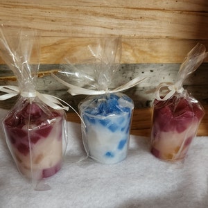 May include: Three small votive candles in clear plastic packaging. The candles are in shades of pink, blue, and white with a marbled effect.