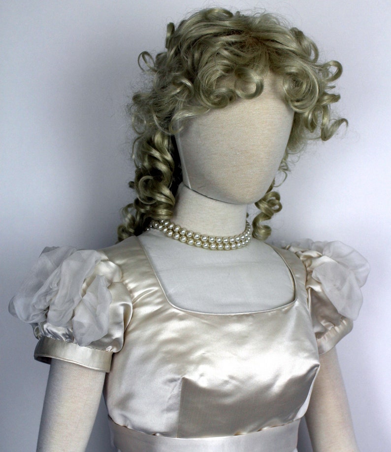 May include: A white satin dress with puffed sleeves and a pearl necklace. The dress has a square neckline and a fitted bodice.