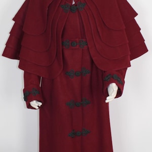 May include: A long, burgundy wool coat with a large, layered cape. The coat has black lace trim and decorative buttons.