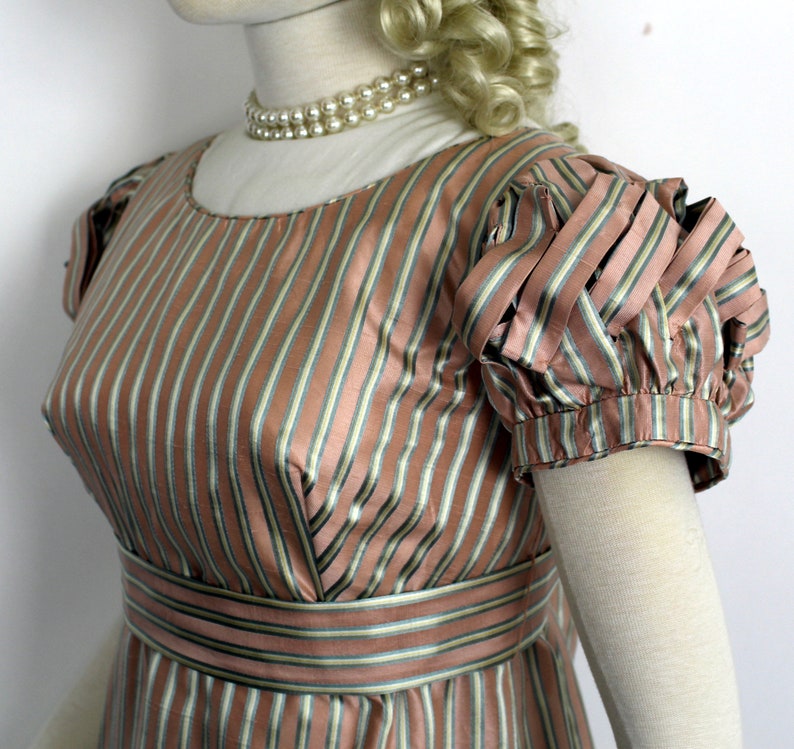May include: A pink and green striped dress with a fitted bodice and short puffed sleeves. The dress has a simple neckline and a narrow belt.