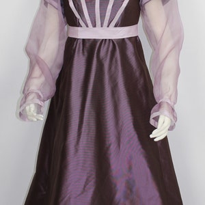 May include: A purple and pink dress with sheer sleeves and a fitted bodice. The dress has a simple, elegant design.