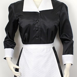 Peut inclure: Une tenue de femme de chambre noire et blanche avec un col blanc, des poignets blancs et un tablier blanc. La tenue a un devant boutonné et une jupe.