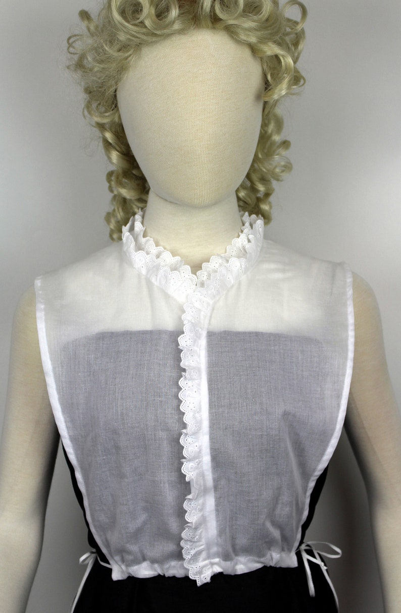 May include: White cotton lace collar with a ruffled edge. The collar is sleeveless and has a button closure in the front.