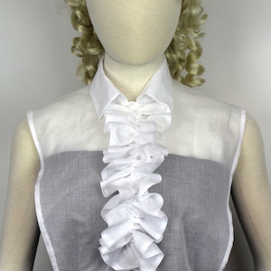 May include: A white sheer blouse with a ruffled collar and a gathered waist. The blouse is sleeveless and has a black undershirt.