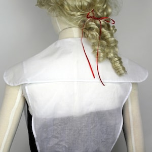 May include: White cotton blouse with a wide, rounded collar and a gathered waist. The blouse is sleeveless and has a simple, elegant design.