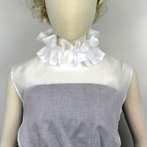 May include: White ruffled collar with a white sleeveless top with a gathered bottom.