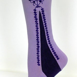 May include: A pair of lavender-colored tights with a dark purple embroidered design on the back of the calf. The design features a floral motif with a long, pointed shape extending down the leg.
