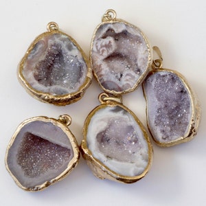 May include: Five gold-rimmed agate crystal pendants with a white and purple interior. The crystals are all different shapes and sizes.