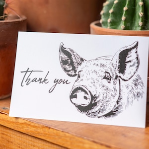 May include: A white card with black ink reads "thank you" and features a black and white illustration of a pig's face.