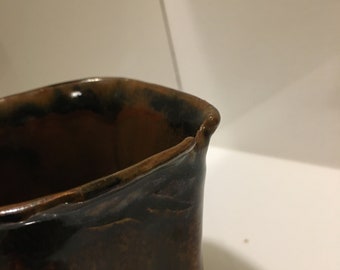 May include: A brown ceramic vase with a slightly uneven rim. The vase has a dark brown glaze with streaks of lighter brown.
