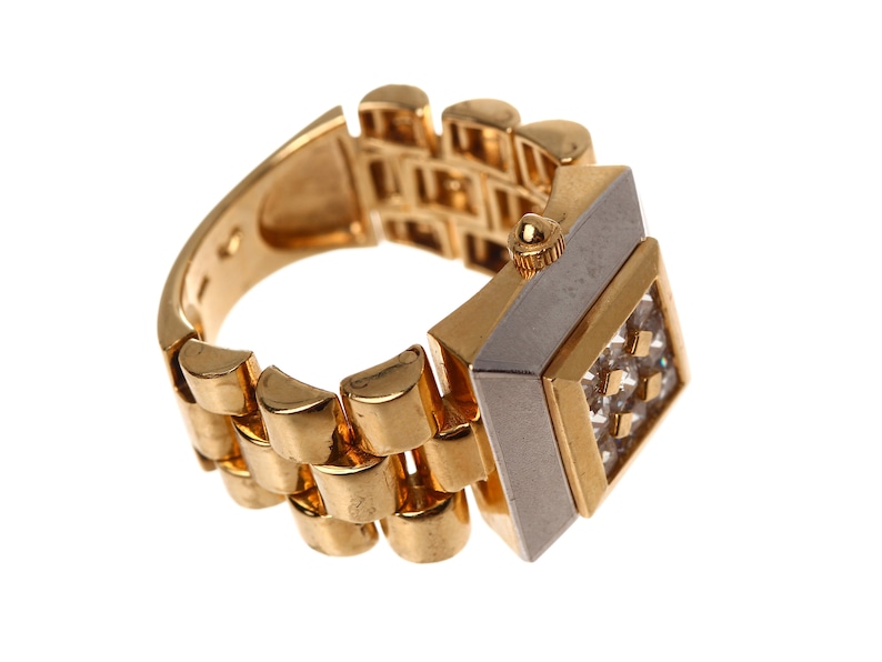 May include: A gold watch ring with a square face and a band that looks like a watch band. The face is set with small clear stones.