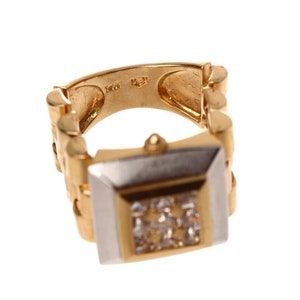 May include: A gold and white watch ring with a square face and a diamond-like stone in the centre. The band is a linked chain style.