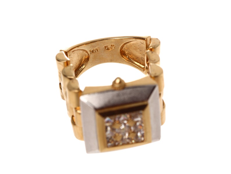 May include: A gold and white watch ring with a square face and a diamond-like stone in the centre. The band is a linked chain style.